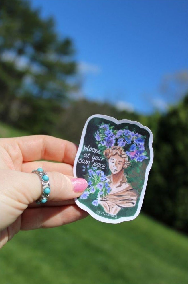 Hand holding a sticker with a woman's face and flowers against a natural background