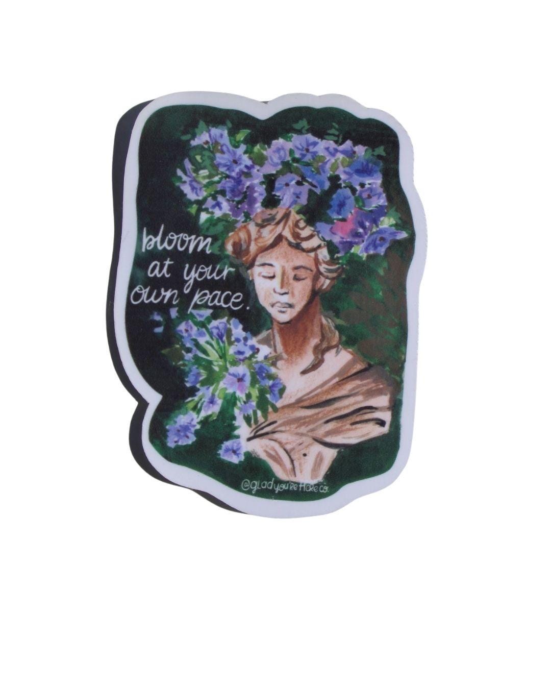 Sticker with a design of a woman with flowers and text 'bloom at your own pace' on a white background.