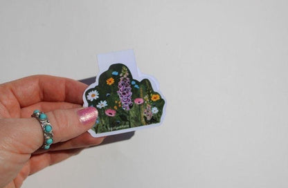 Hand holding a floral magnetic bookmark against a light gray background
