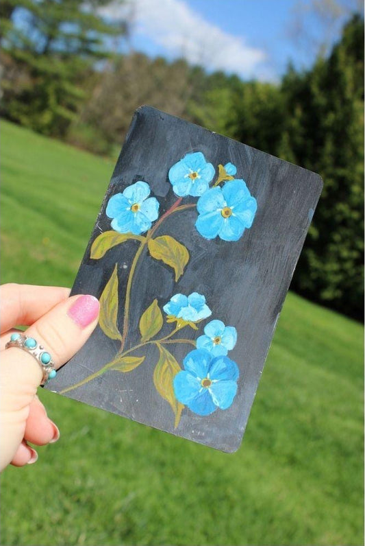 Hand holding a playing card with blue forget me nots design against a natural background