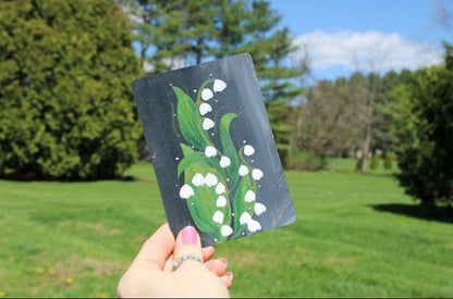 Hand holding a card with a floral design outdoors on a sunny day