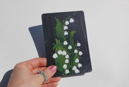 Hand holding a black card with a white flower design against a plain background