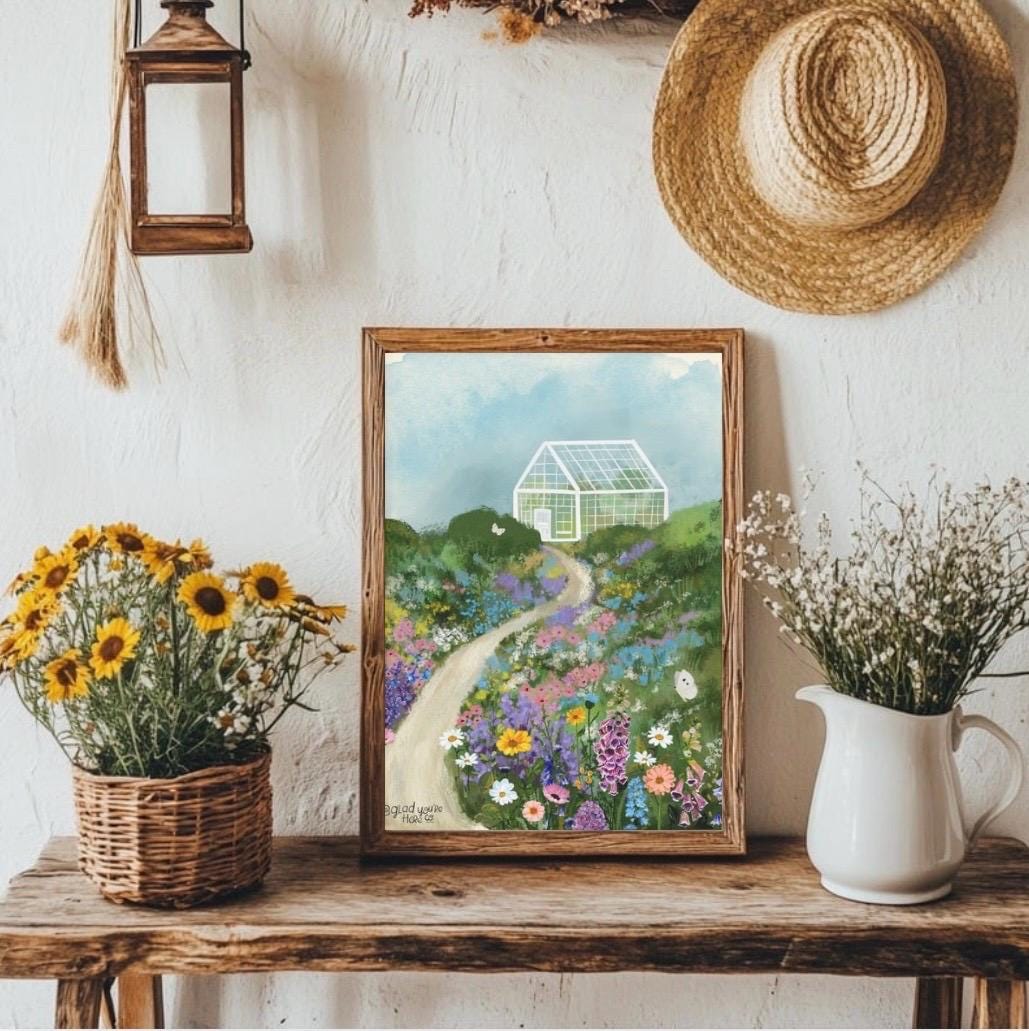 Framed artwork of a garden scene on a wooden table with flowers and a hat in the background.