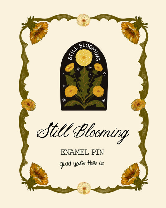 Enamel pin with floral design and 'Still Blooming' text on a beige background