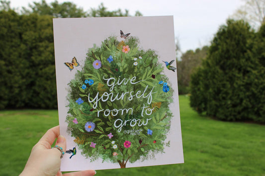 Card with a tree illustration and 'Give yourself room to grow' text held in front of a garden.