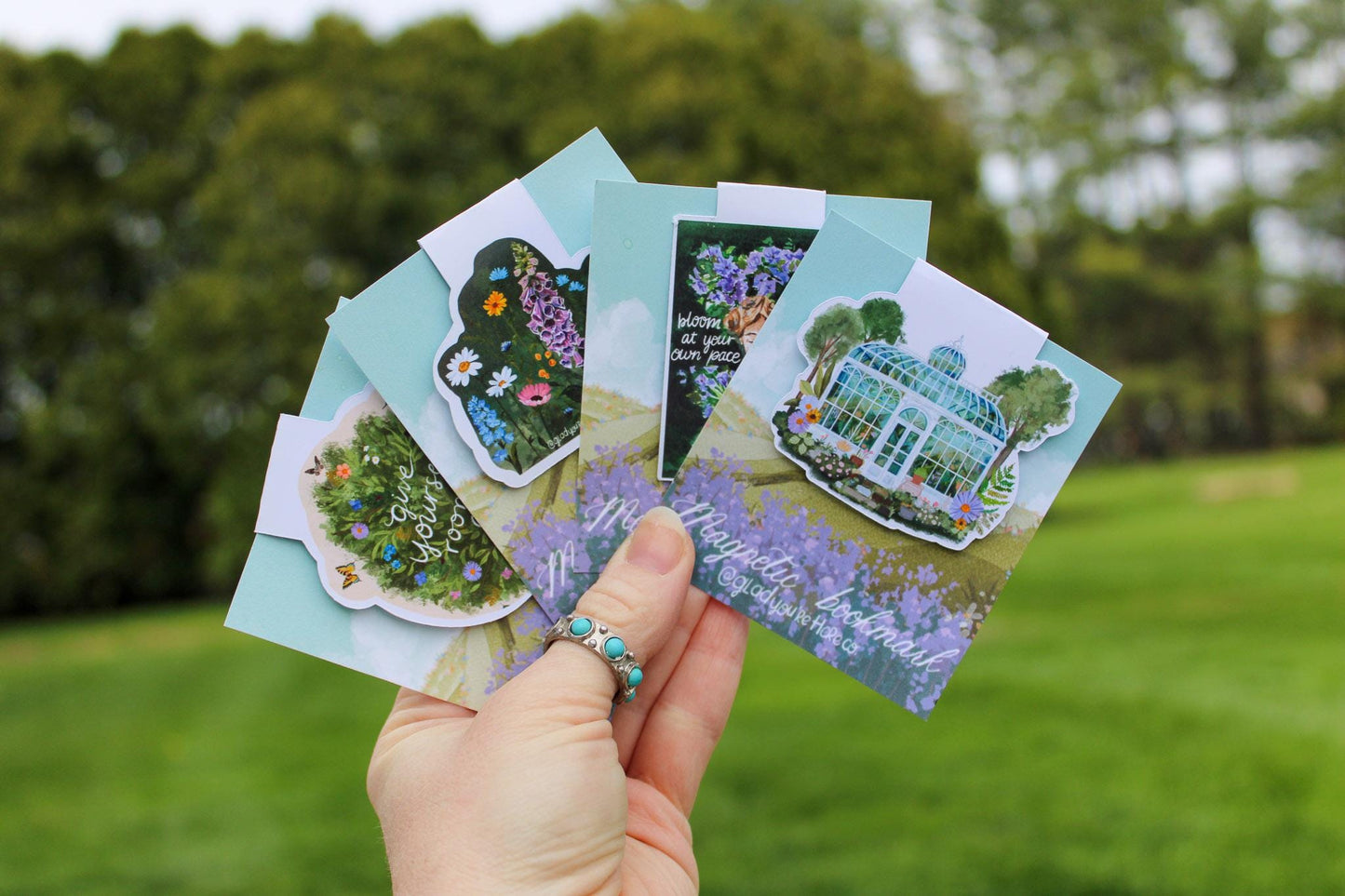Hand holding a set of garden-themed cards with a blurred green outdoor background