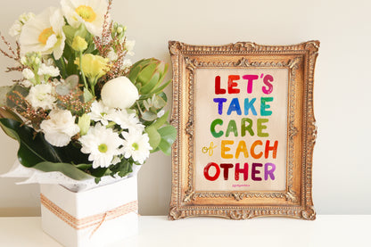 Decorative framed print with colorful text 'Let's take care of each other' next to a bouquet of flowers.