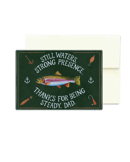 A rectangular dark green greeting card with a trout illustration and fishing-themed text reading 'Still Waters Strong Presence Thanks for Being Steady, Dad,' shown with a plain white envelope behind it on a white background.