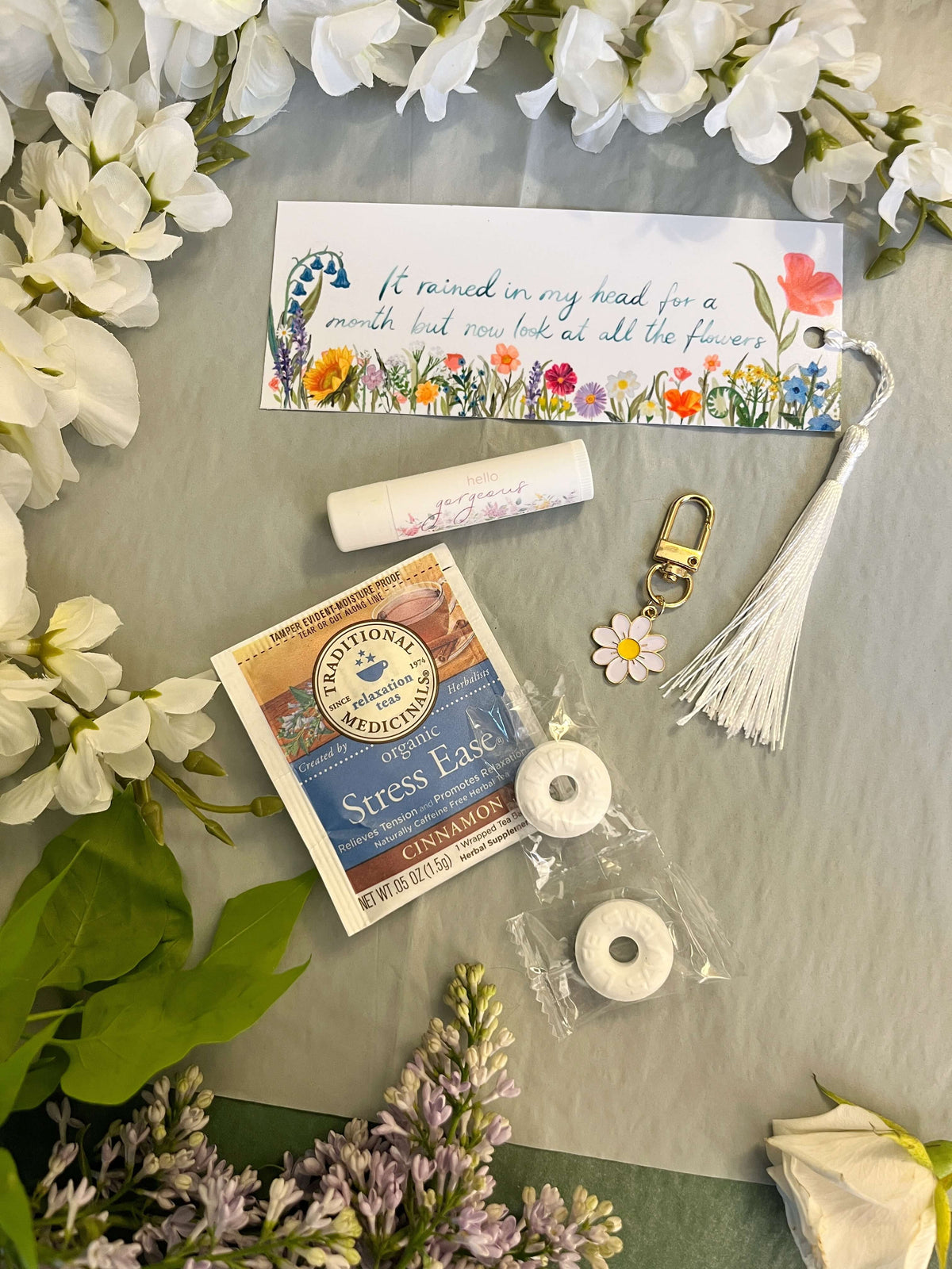 Assorted items including a stress relief kit, lip balm, and keychain on a surface with flowers around.