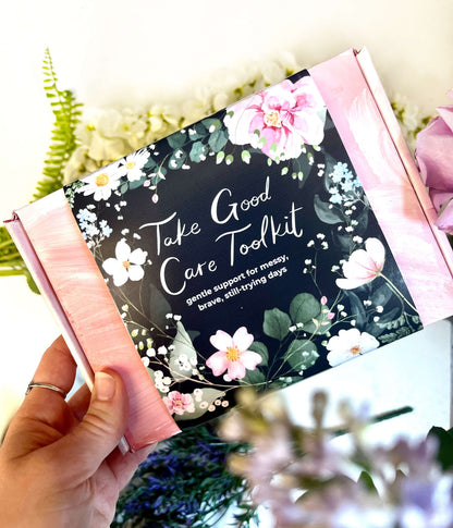 Hand holding a 'Take Good Care Toolkit' with floral design and text.