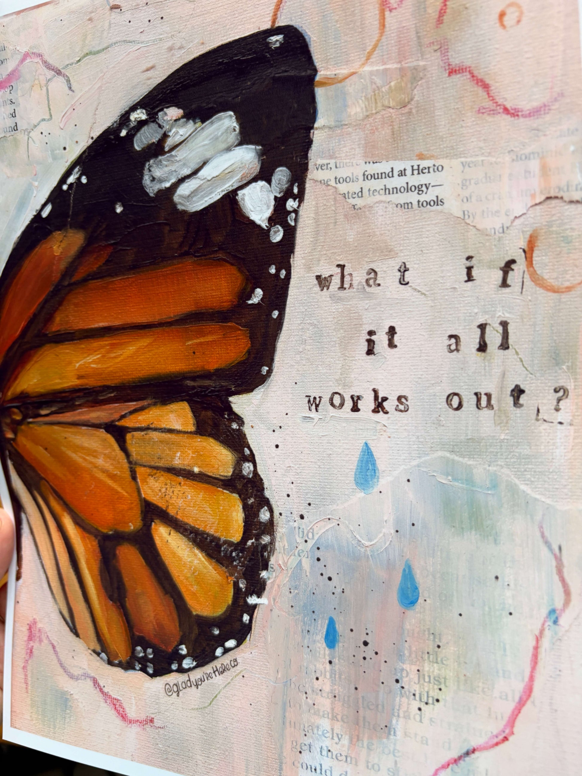 A close-up of a mixed-media painting featuring a large orange and black monarch butterfly wing on the left, with the text 'what if it all works out?' on a textured cream background with blue raindrop accents.