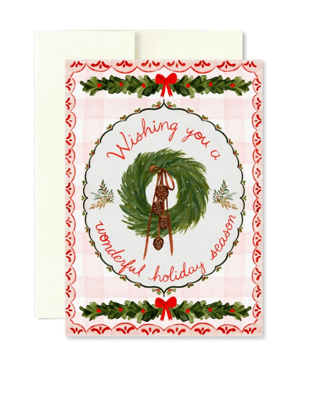 A Christmas greeting card with a white envelope behind it. The card features a light pink gingham background, a red border pattern, and a central illustration of a green wreath with a brown ornament, surrounded by the words 'Wishing you a wonderful holiday season' in red script.