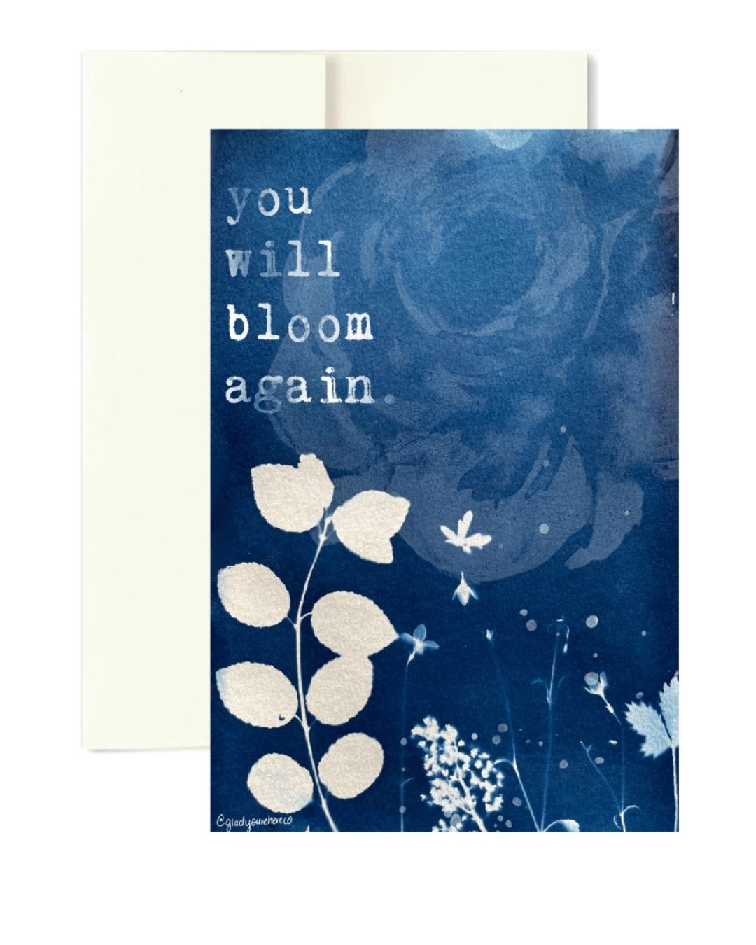 A blue greeting card with the printed message 'you will bloom again' in white typewriter-style text, shown with a white envelope behind it on a white background.